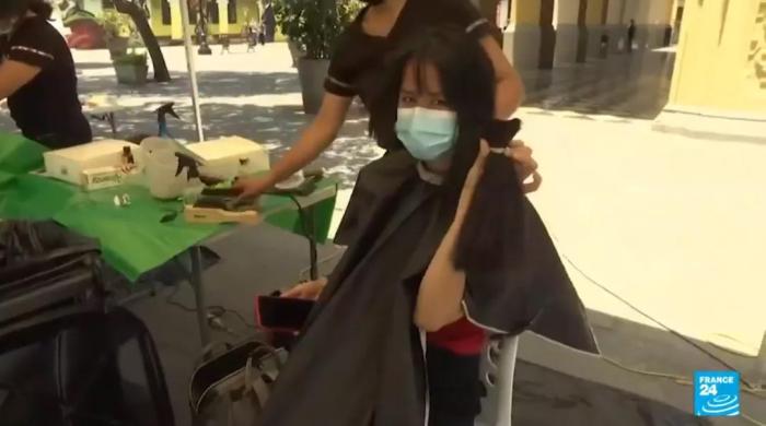秘鲁女子在街头剪去长发后，手拿剪掉的头发向镜头展示。图片来源：法国24小时新闻台报道截图