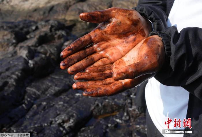 当地时间1月18日，秘鲁Callao，一名路人查看污染情况，展示沾满油污的双手。