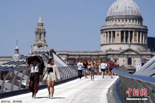 热浪来袭，人们在伦敦千禧桥上遮挡太阳前行。图片来源：中国新闻网
