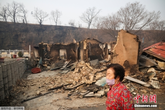 图为当地时间3月27日,韩国庆尚北道义城郡,一名妇女走在被烧毁的房屋前。 article_img